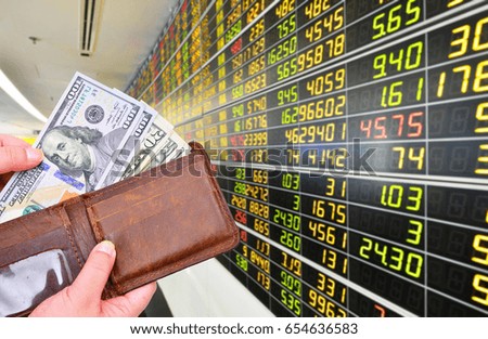Man's hand holding Dollar (USD) banknotes  with brown wallet on monitor stock market background.