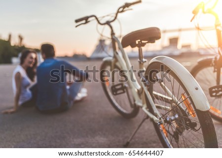 Beautiful romantic couple is having rest in the city with bicycles on the sunset. Enjoying the company of each other. Bicycle is on the foreground