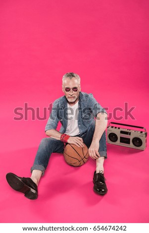 senior man sitting on floor with tape recorder and basketball ball isolated on pink