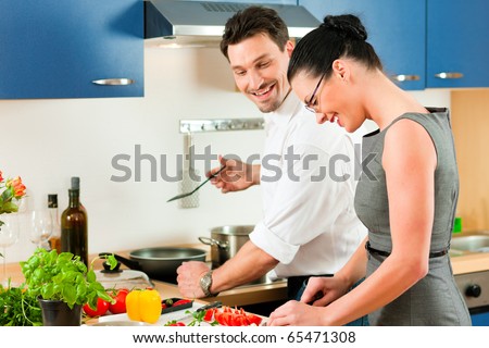 Young couple cooking - man and woman in their kitchen at home preparing vegetables for salad and pasta sauce Royalty-Free Stock Photo #65471308