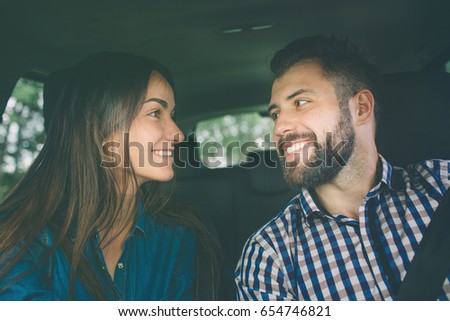 Careful driving. Beautiful young couple sitting on the front passenger seats and smiling while handsome man driving a car