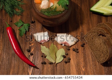 Russian soup in a clay pot among vegetables, herbs and spices