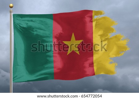 Cameroon flag with torn edges in front of a stormy sky