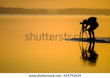 A silhouette view of a photographer during golden hour with a reflection on the water