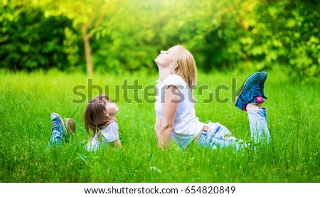 Beautiful little girl and woman, has blonde and haired hair, dressed in white t-shirt, blue jeans. Family portrait. Mom and daughter. Sport meditation. Yoga concept.