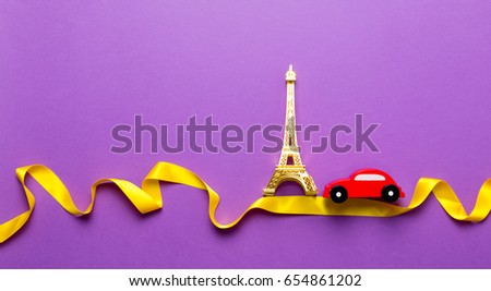 Little toy car with Eiffel tower moving over twisted ribbon on purple background