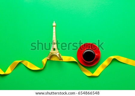 Cup of coffee and Eiffel tower toy on green background