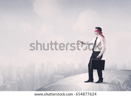 Young blindfolded businessman steps on a grey world map with a city in the background