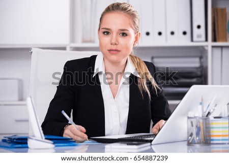Young smiling businesswoman sitting at working place in office