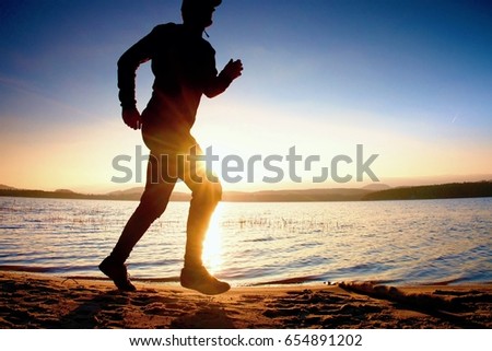 Training at sunset. A silhouette of jogger body  at path along lake coastline.
