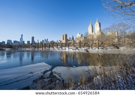 Scenic view of the Upper West Side skyline reflecting in the ice of the frozen Central Park lake the morning after a winter snow storm in New York City