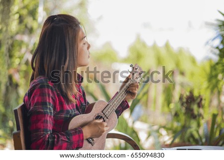 Young hipster woman sitting playing ukulele guitar at home in garden.