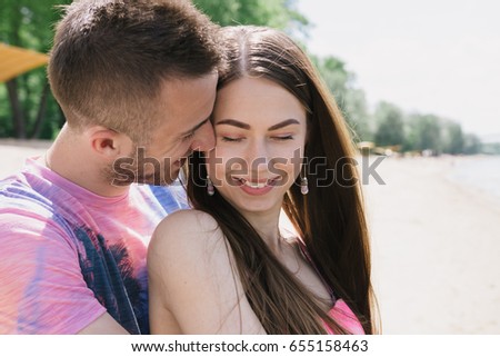Young couple hugging and smiling at each other on the river bank. Walking along the sandy beach.