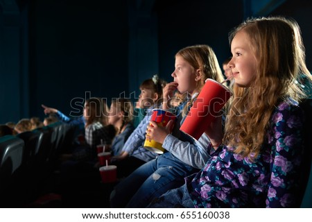 Cute young girl smiling joyfully sipping her drink watching a movie at the cinema copyspace entertainment positivity children childhood relax activity leisure hobby beverage snack concept.