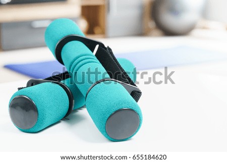 Fitness at home concept, a pair of green dumbbells in the foreground and an fitness ball in the background.
