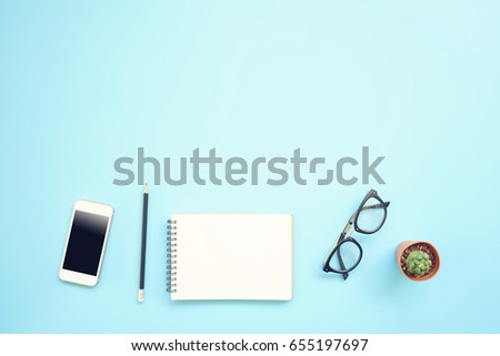 Flat lay design of work desk with blank notebook pencil glasses smartphone and cactus on blue background. 