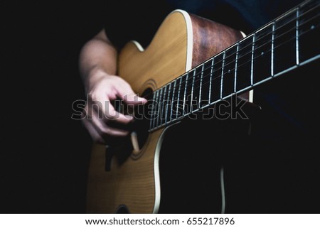 Guitar with a man's hands playing the guitar in the dark background, black space left for the text.