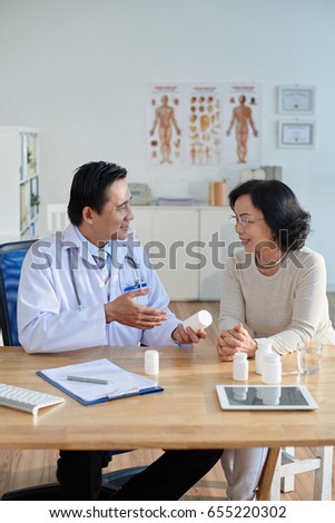 Wait-up portrait of friendly doctor sitting at desk and prescribing drugs to pretty senior patient