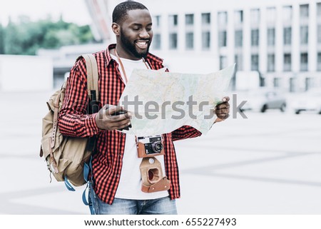 Handsome and happy Afro American tourist with old camera and map in modern city
