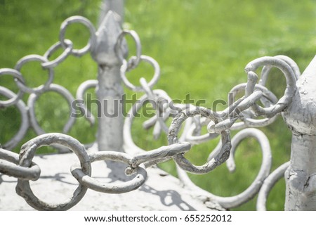 Elements of a light gray metal fence with chains. Closeup, selective focus.