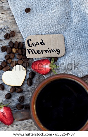 A cup of espresso on a wooden background. Coffee beans, strawberries, picture "Good Morning". Breakfast, coffee on the nature.
