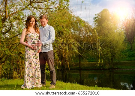 Young Happy pregnant woman and her husband in the park at sunset. Waiting for baby