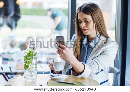 Beautiful Young Woman Drinking Coffee and Looking at her phone