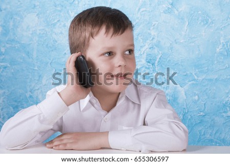 A little cute little boy is talking on the phone. A boy in a white shirt on a blue background.

