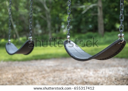 An empty pair of swings hang at the playground. No children are playing on the swing set, which is not moving.  The swings are clean and well maintained.  Back to School. Recess equipment. Outdoors.  Royalty-Free Stock Photo #655317412
