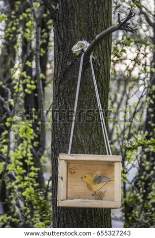 A birdhouse with a chalk drawing yellow bird hanging on a tree on the background of forest