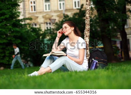 Smiling girl student in city park with book on the background of a university building