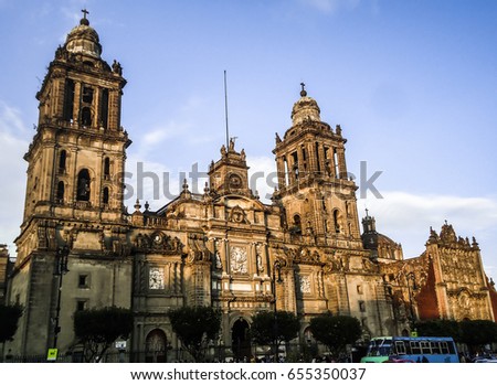 Front exterior and ancient towers of the Metropolitan Cathedral of the Assumption of Virgin Mary on the Plaza de la Constitución (Zócalo)in the old town of Mexico City, CDMX, México. Royalty-Free Stock Photo #655350037