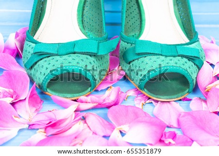 Green shoes on the petals of roses. Blue wooden background