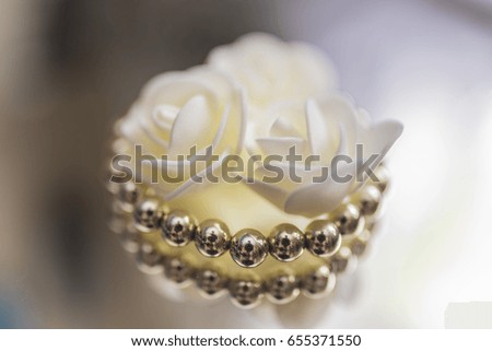 A gold bracelet lies around small white roses on a mirror surface on a light blurred background