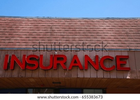 Insurance in Giant Red Letters Mounted on Brown Wood Beneath a Tiled Roof in a Shopping Center in a Sunny Afternoon under a Clear Blue Sky