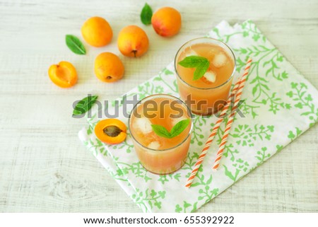 Apricot juice with ice cubes and apricots on a light background. Horizontal. Selective focus. View from above.