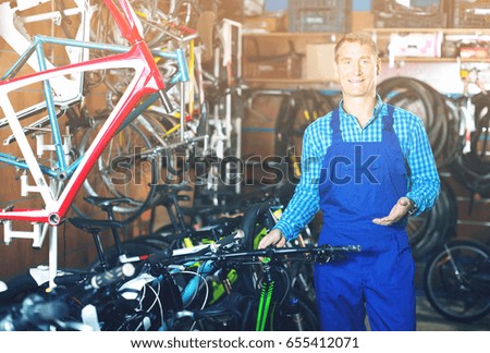 friendly smiling man in blue overall working in bicycle shop 
