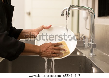 Woman washing the dishes in kitchen sink in the restaurant Royalty-Free Stock Photo #655414147
