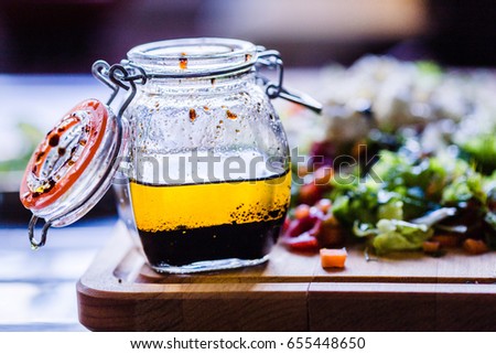 A Glass Bottle with Salad Dressing consisting of Balsamic Vinegar, Olive Oil, Pepper and Salt, Salad on the Background, Horizontal View Royalty-Free Stock Photo #655448650