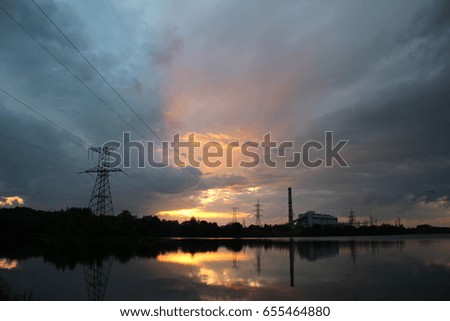 Power station on the shore of the lake in the rays of the setting sun. Sunset, evening, clouds.