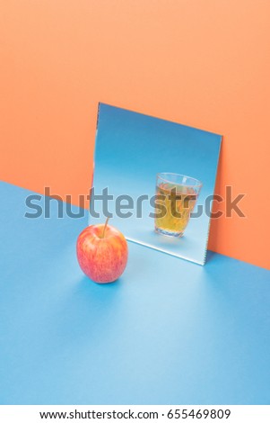 Picture of apple near glass with juice in mirror on blue table isolated over orange background.