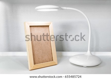 Vertical wooden picture frame and modern lamp decoration on white shelf