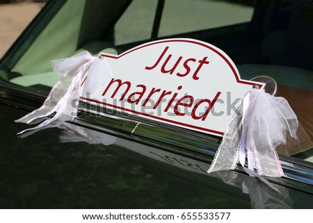 "Just married" sign in red letters on white attached to a sedan luxury car