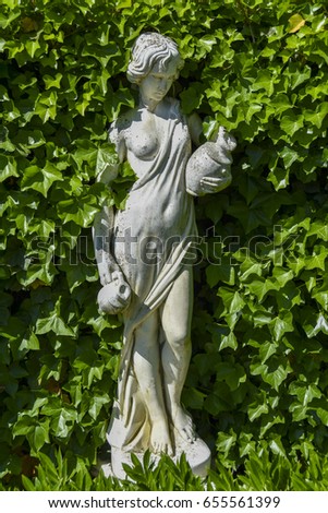 A white sculpture surrounded by leafs in a natural framing. Classical Greek ornament with a woman and a pitcher.