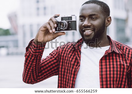 Outdoor summer smiling lifestyle portrait of handsome and happy Afro American tourist  having fun in the city in Europe with camera travel photo of photographer making pictures in hipster style