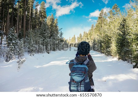 A female hiker is taking a picture of trail in the forest and snow.