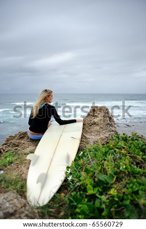 Female surfer sitting on cliffside with surfboard