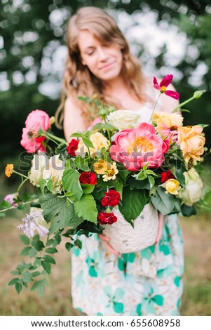 floral design, wedding, decoration, occasion concept - pretty woman in summer dress puting out grand bouquet of various flowers: big pink peonies, tender avalanches and carnations