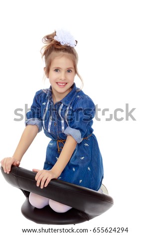 The little blonde girl with a large white bow on the head and short denim dress.She poses on a revolving chair.Isolated on white background.