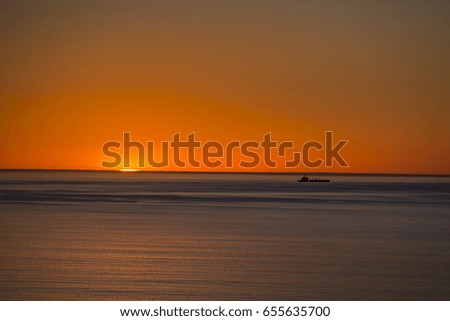 A minimalistic shot of a cargo ship on the horizon of the ocean at sunset
